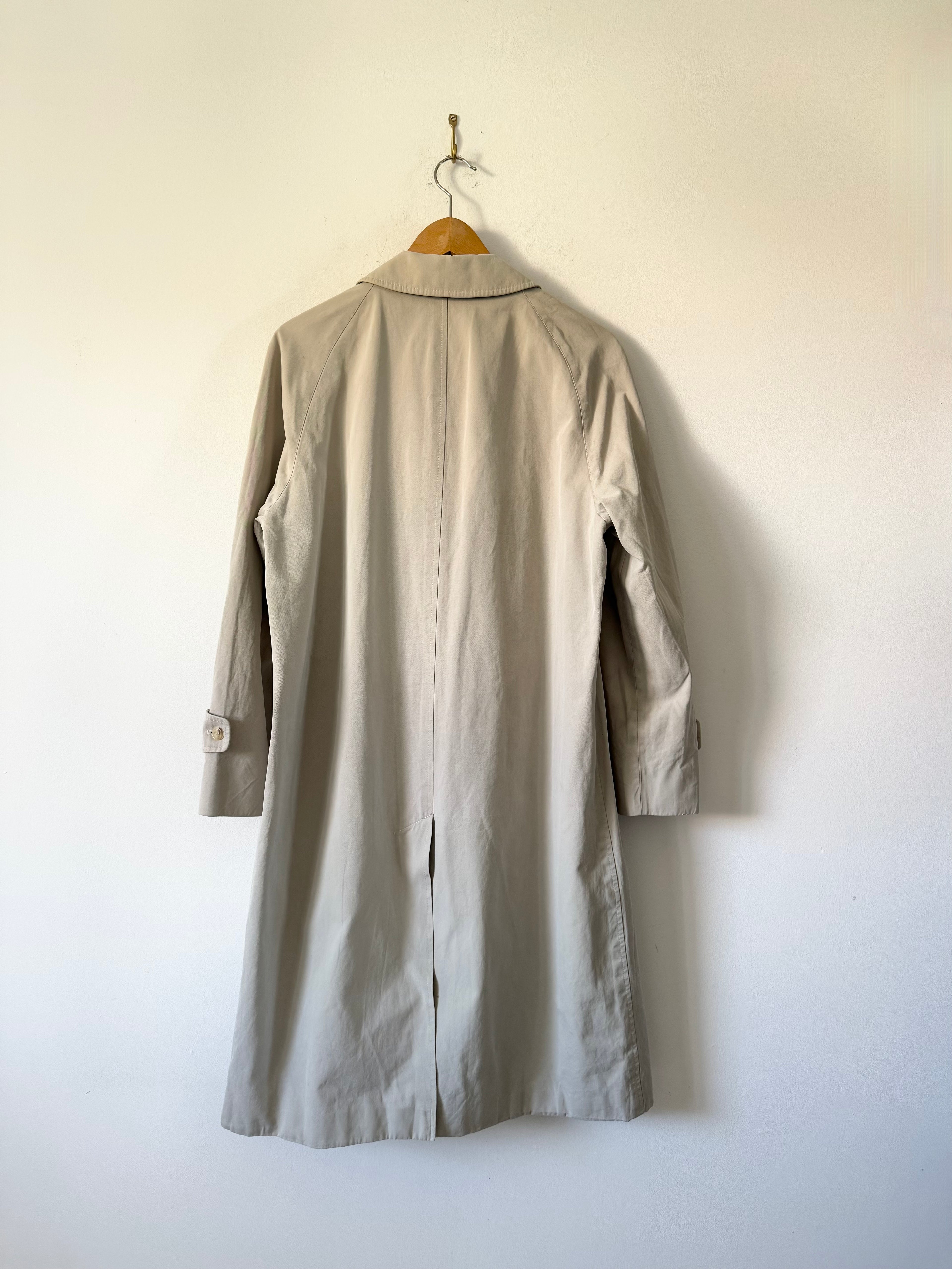 Beige coat hanging on a wooden hanger against a white wall