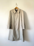 Beige trench coat hanging on a hanger against a white wall