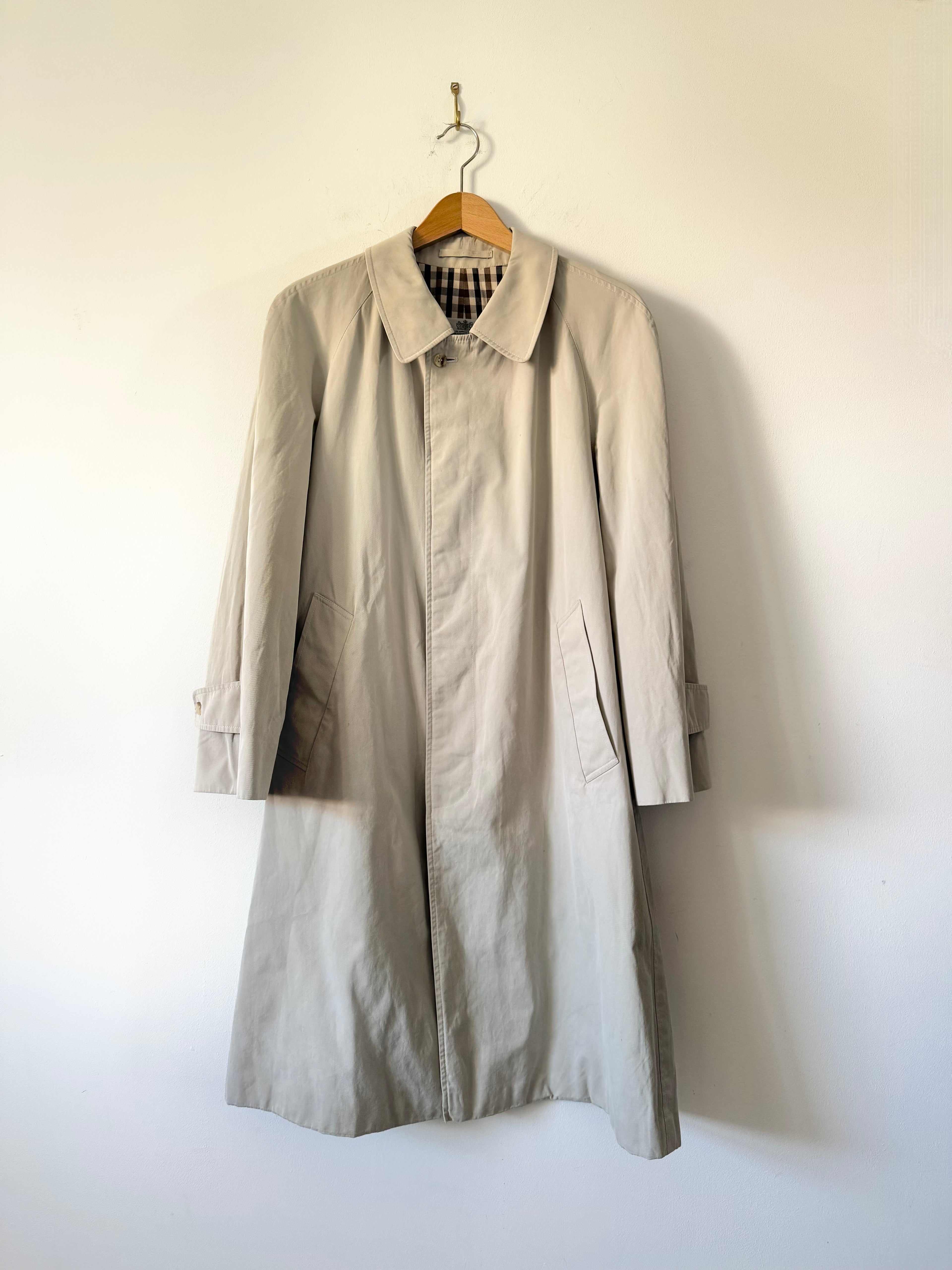 Beige trench coat hanging on a hanger against a white wall