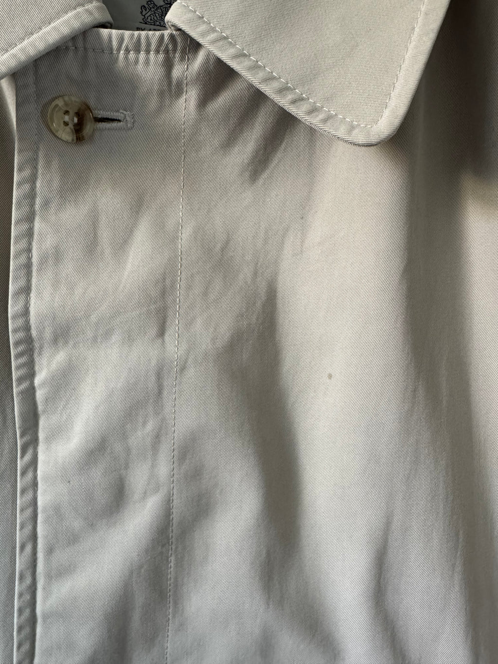 Close-up of a beige trench with a button, showing texture and fabric details.