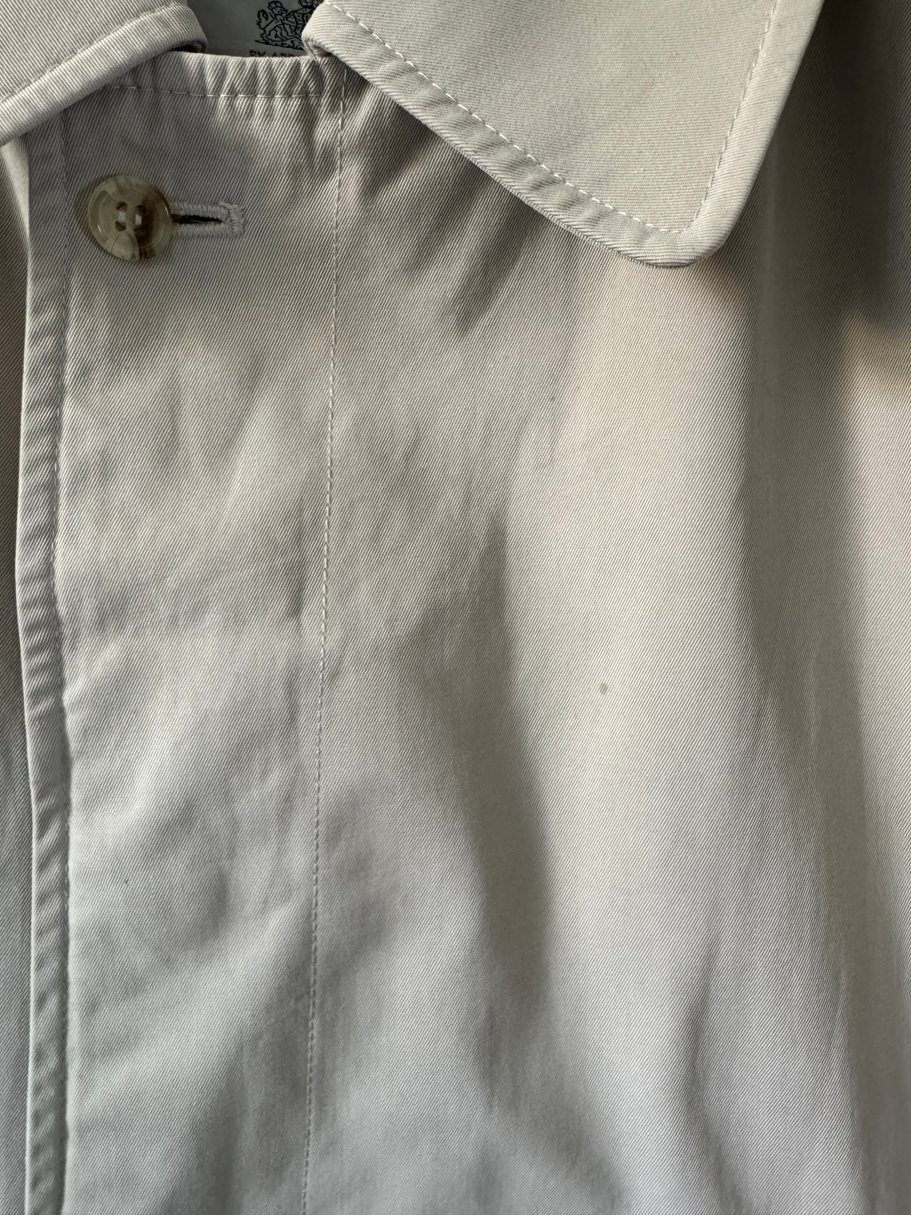 Close-up of a beige trench with a button, showing texture and fabric details.