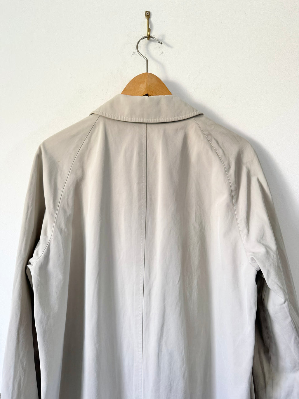 Light beige trench on a wooden hanger against a white wall