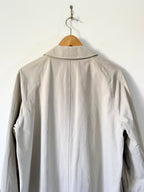 Light beige trench on a wooden hanger against a white wall