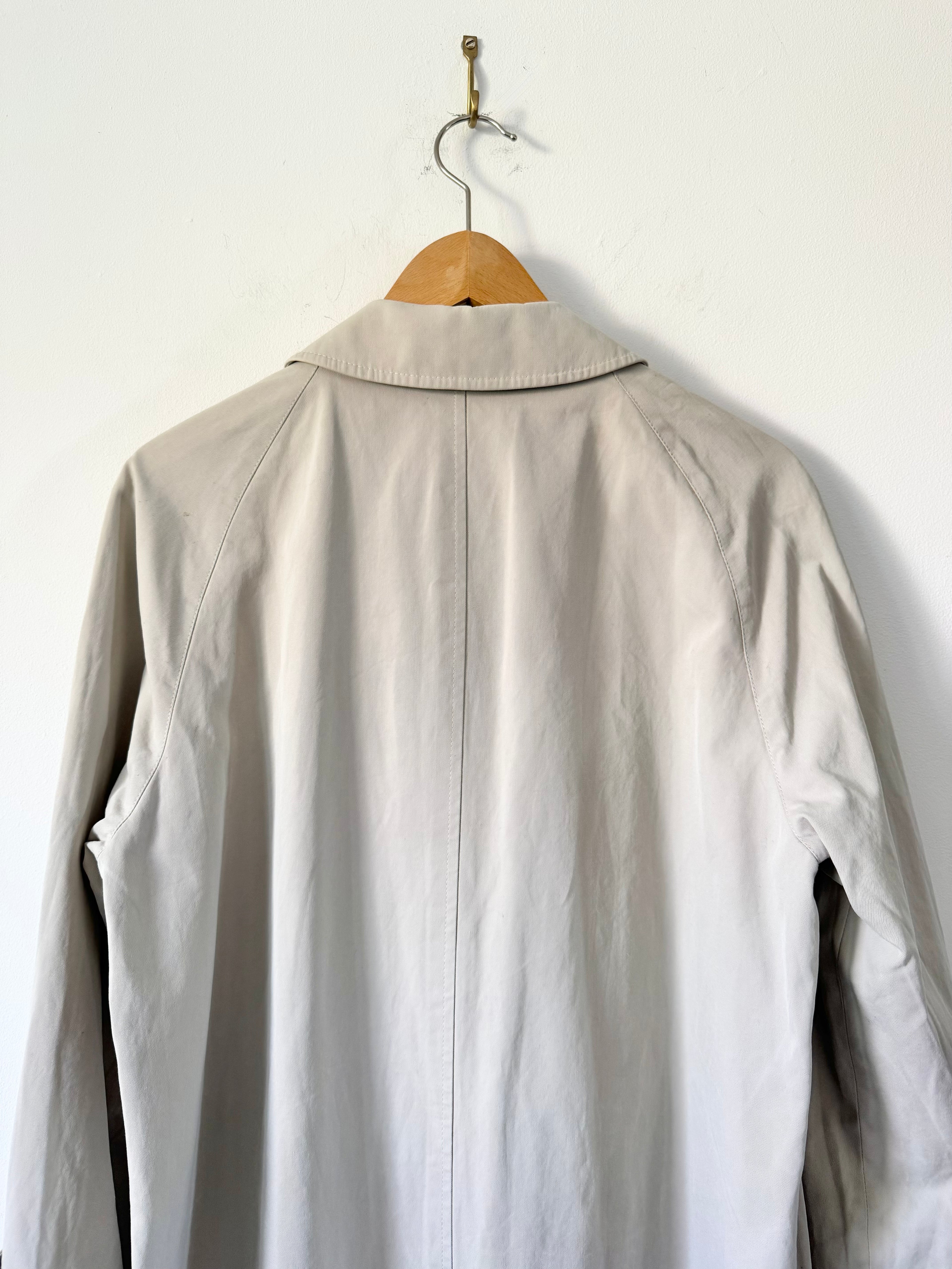 Light beige trench on a wooden hanger against a white wall