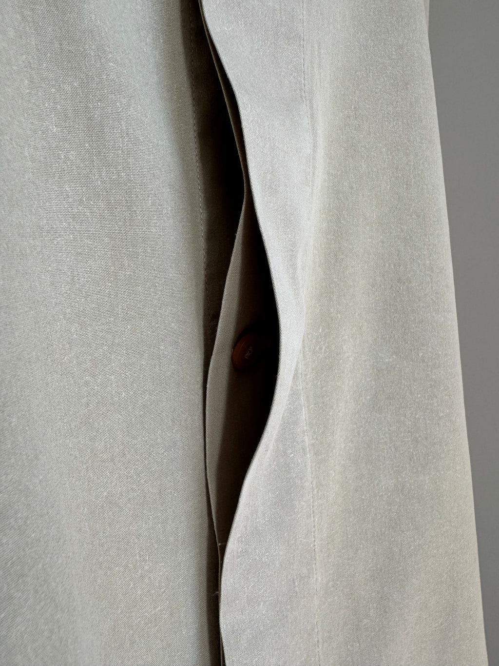 Close-up of a light beige textured fabric garment with a curved opening and a small brown button visible in the center.