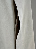 Close-up of a light beige textured fabric garment with a curved opening and a small brown button visible in the center.