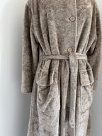 A plush, textured bathrobe in a taupe-brown color, featuring a tie belt, large front patch pockets, and wooden buttons, shown against a plain light gray background.