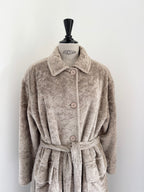 A plush, textured beige bathrobe with a collar, button closure, and matching waist tie, displayed on a mannequin torso against a plain white wall.