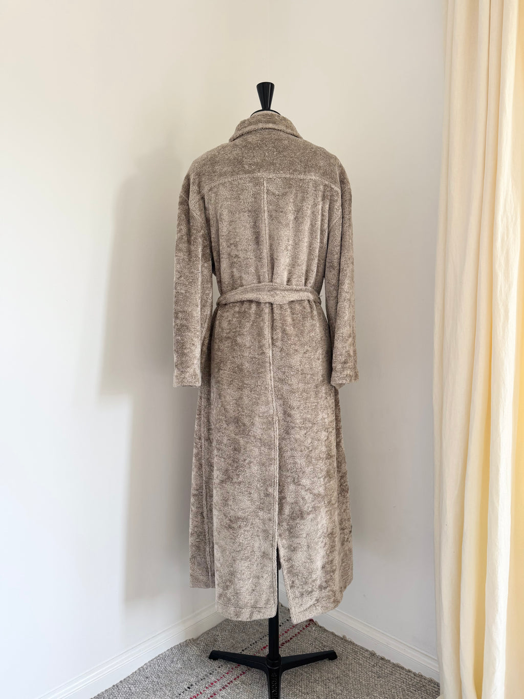 A plush, textured coat in a warm taupe-beige color, shown from the back on a black dress form mannequin.