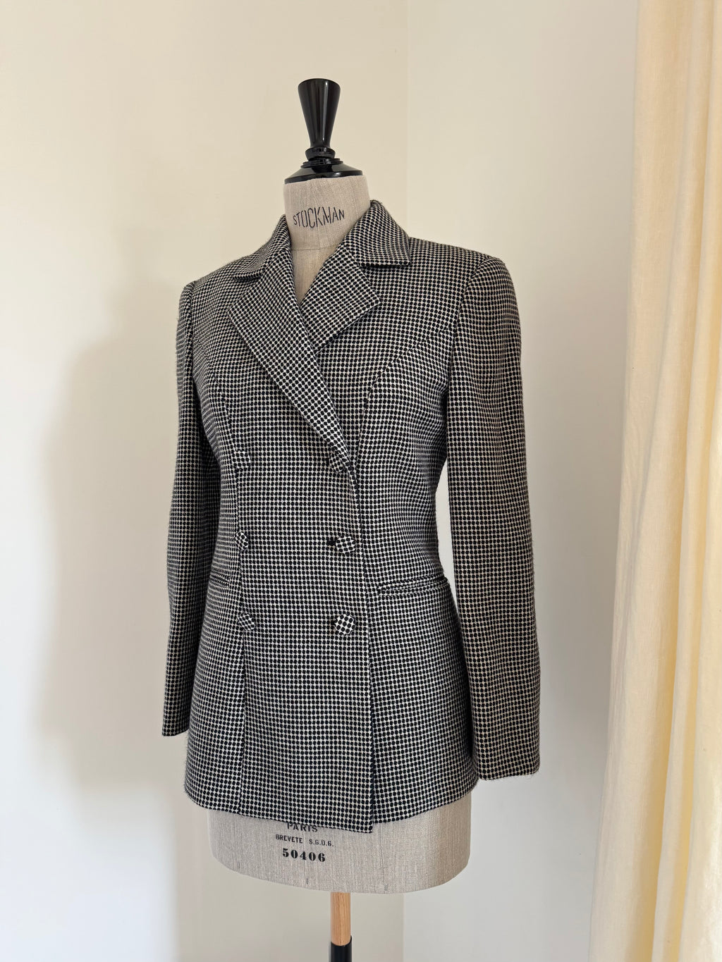 A women's double-breasted blazer in a black and white houndstooth pattern, displayed on a dress form mannequin against a plain off-white wall.