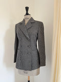 A women's double-breasted blazer in a black and white houndstooth pattern, displayed on a dress form mannequin against a plain off-white wall.