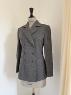 A women's double-breasted blazer in a black and white houndstooth pattern, displayed on a dress form mannequin against a plain off-white wall.