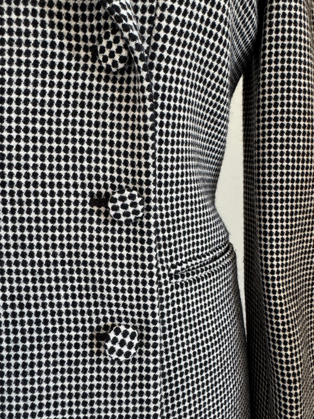 Close-up of a black and white micro-check patterned fabric, showing the texture and a button detail.