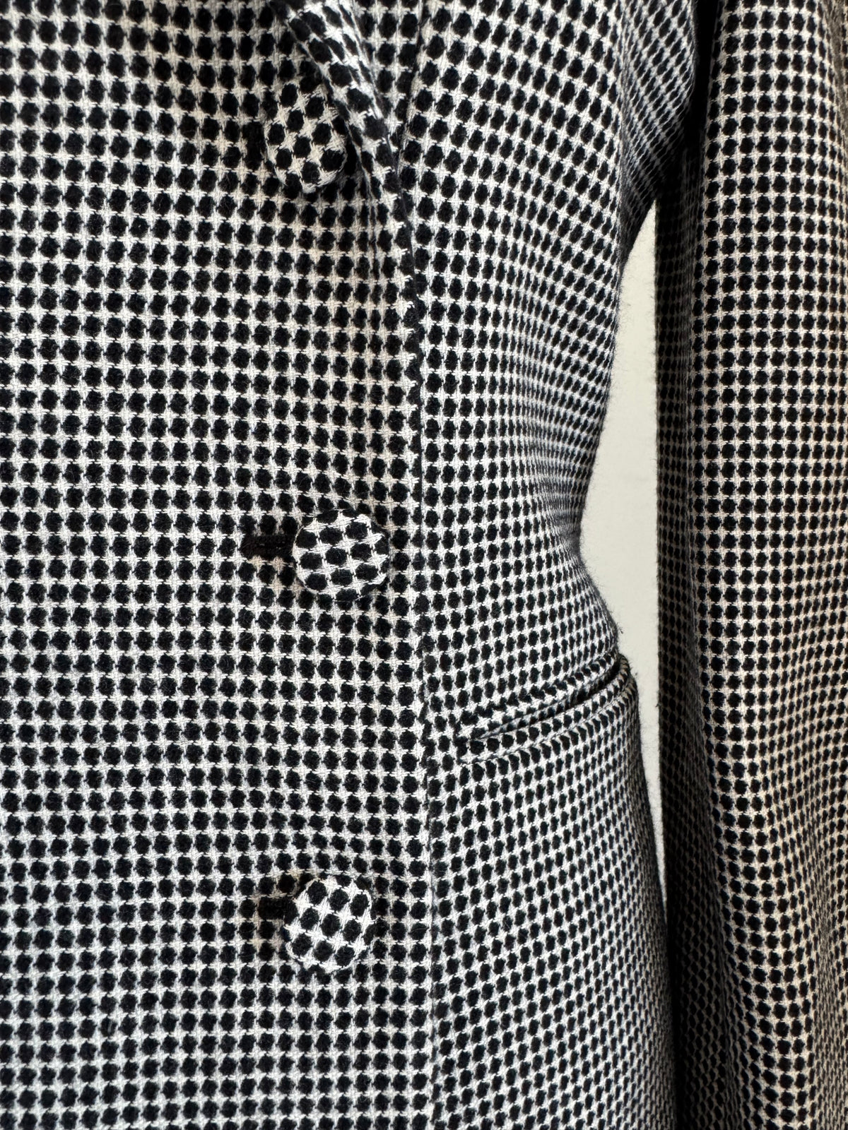 Close-up of a black and white micro-check patterned fabric, showing the texture and a button detail.