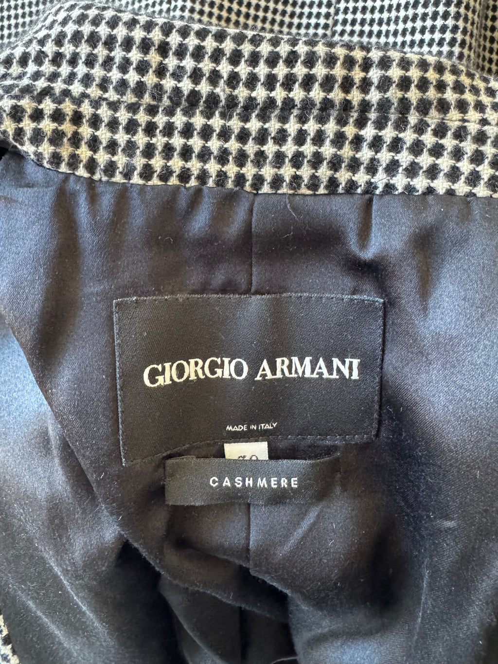 Close-up of a Giorgio Armani garment interior showing a black fabric label with gold lettering that reads 'GIORGIO ARMANI' and a side tag reading 'CASHMERE'.