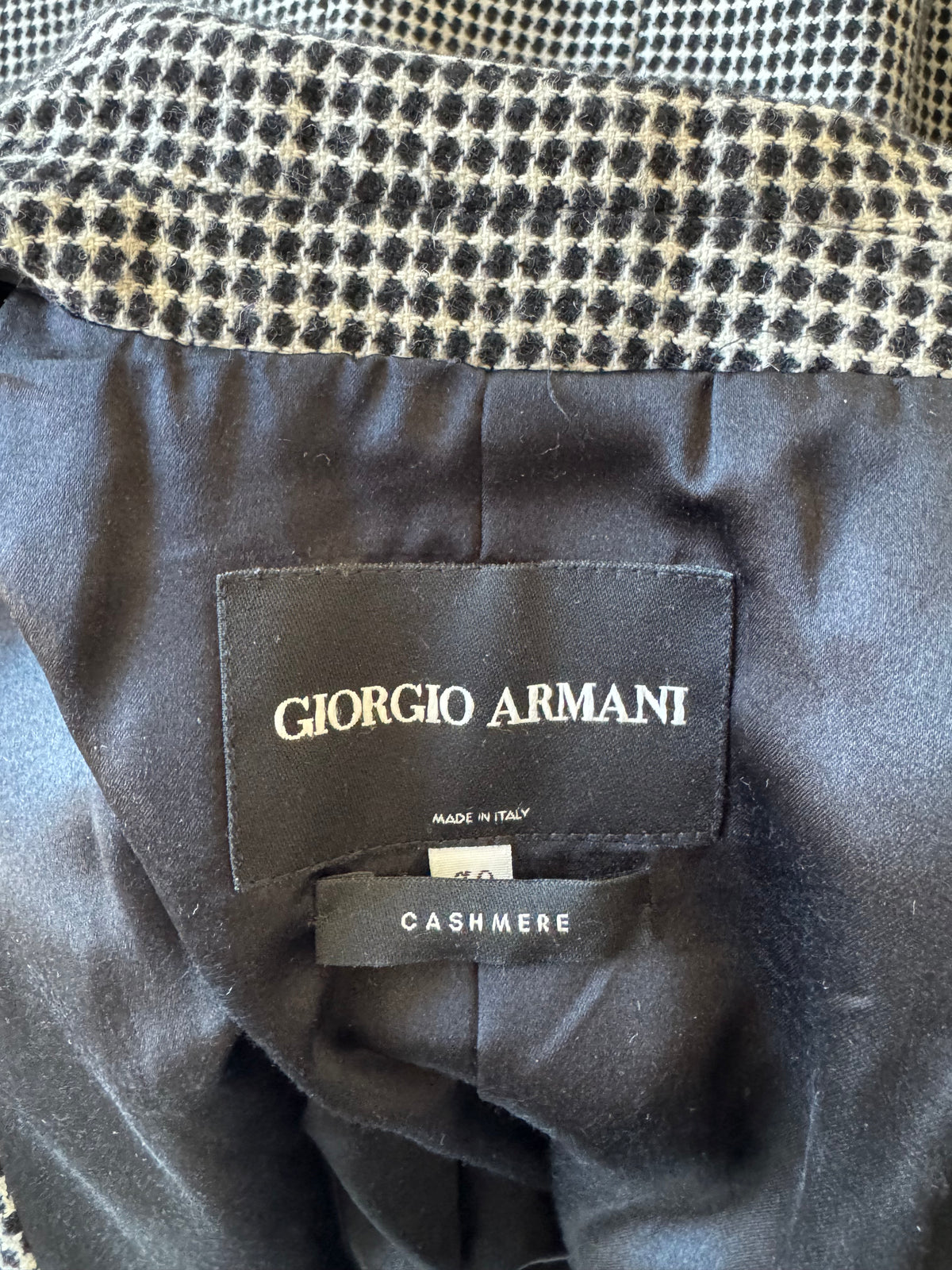Close-up of a Giorgio Armani garment interior showing a black fabric label with gold lettering that reads 'GIORGIO ARMANI' and a side tag reading 'CASHMERE'.