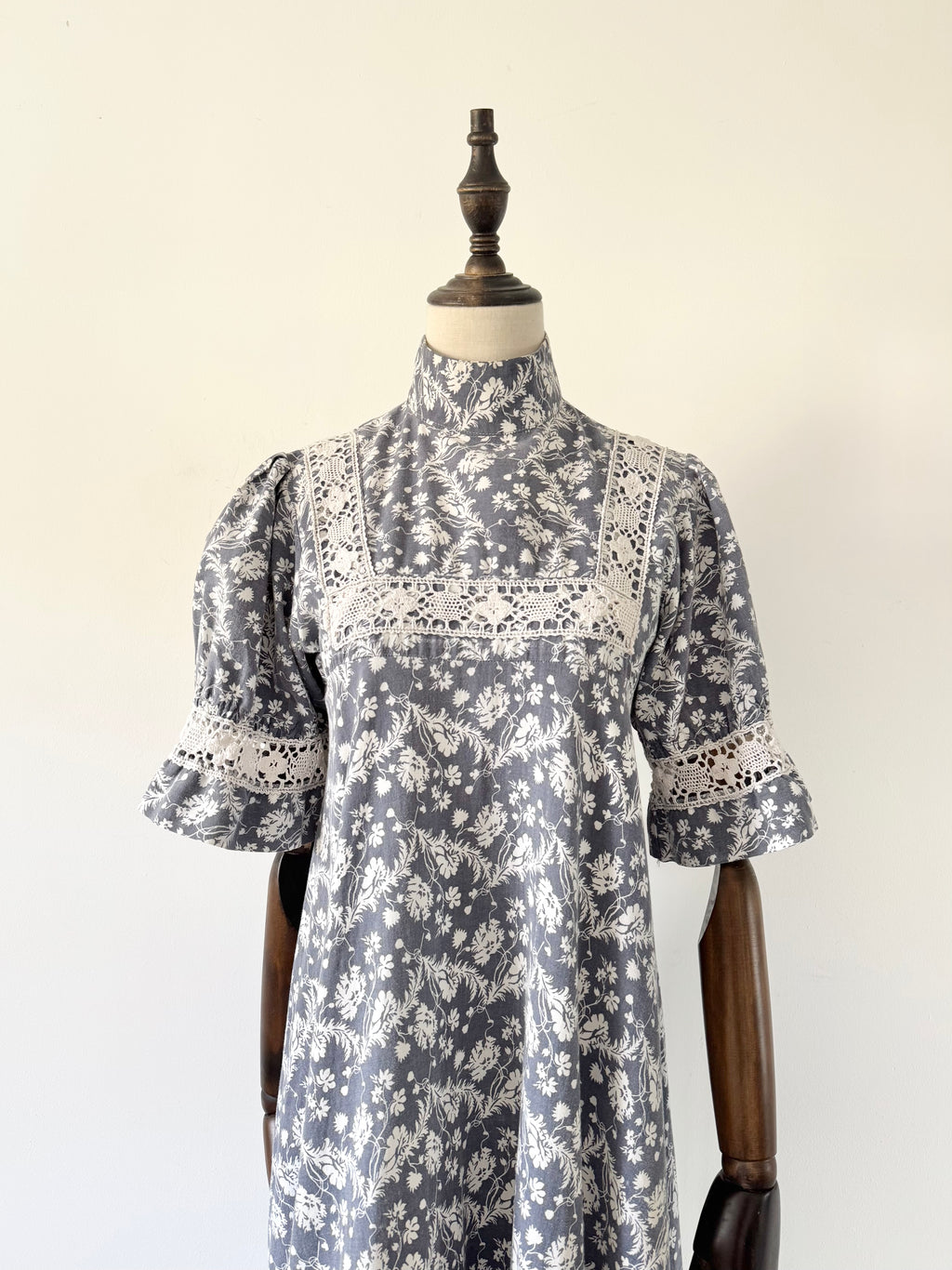 Grey floral dress with white lace details on a mannequin against a plain background