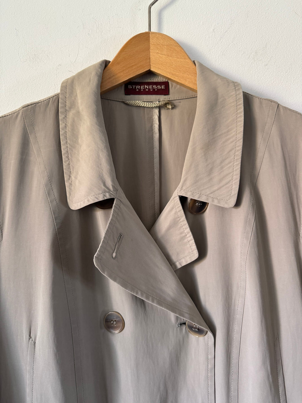 Beige trench coat on a hanger against a white background