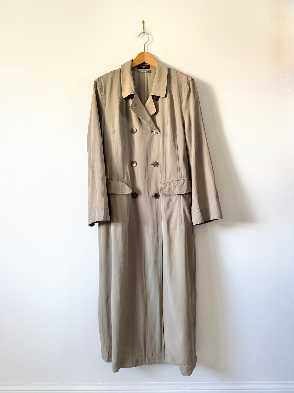 Beige trench coat on a hanger against a white wall