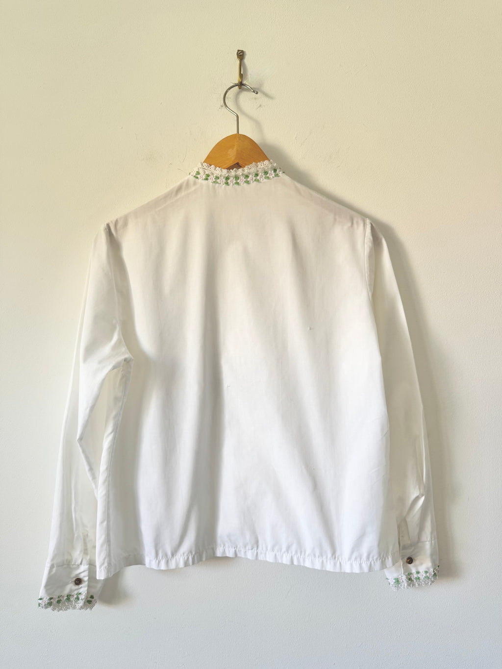 White blouse with lace details on a hanger against a white background
