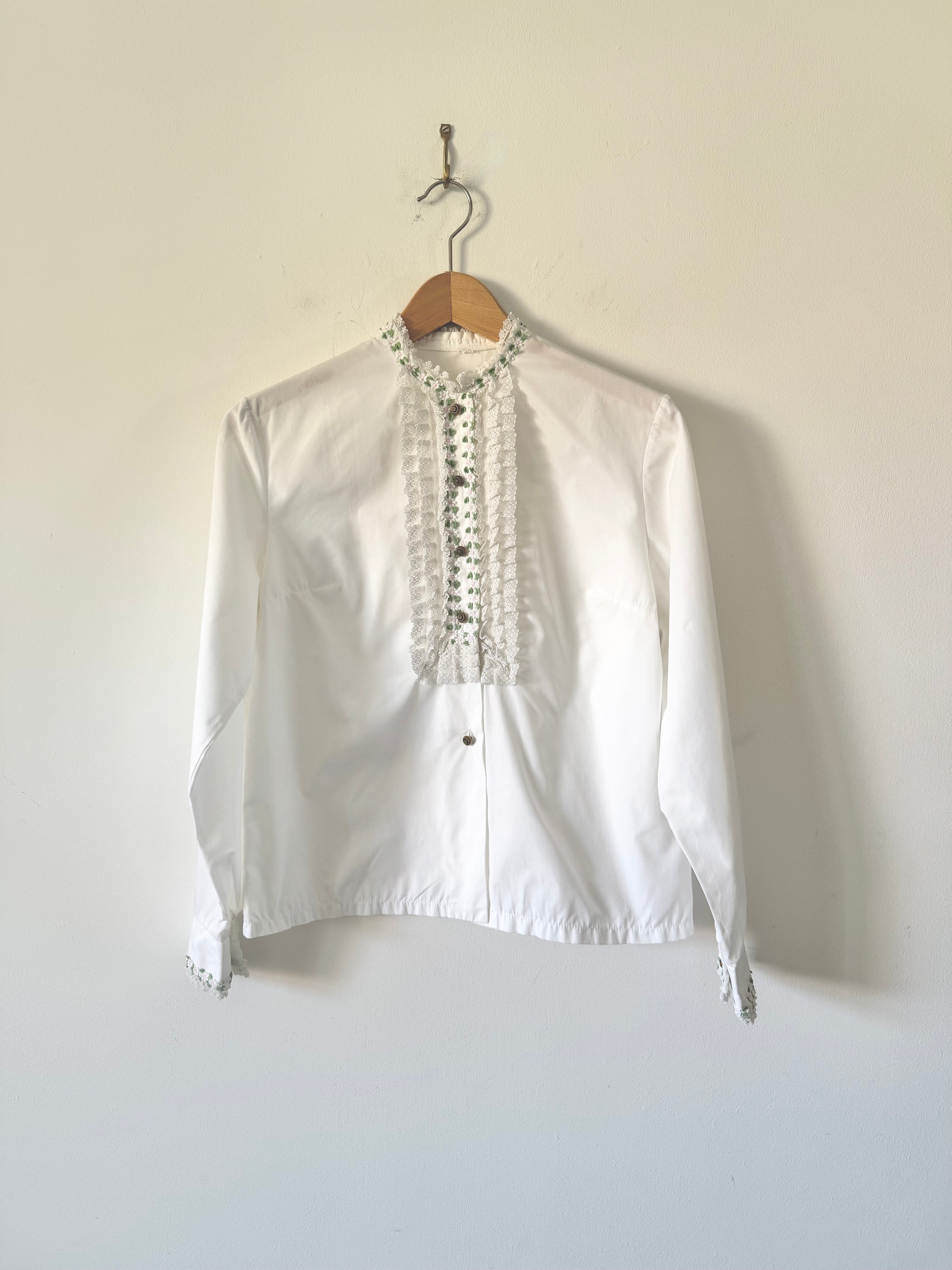 White blouse with lace details on a wooden hanger against a plain background
