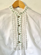 White blouse with floral lace details on a wooden hanger against a white background